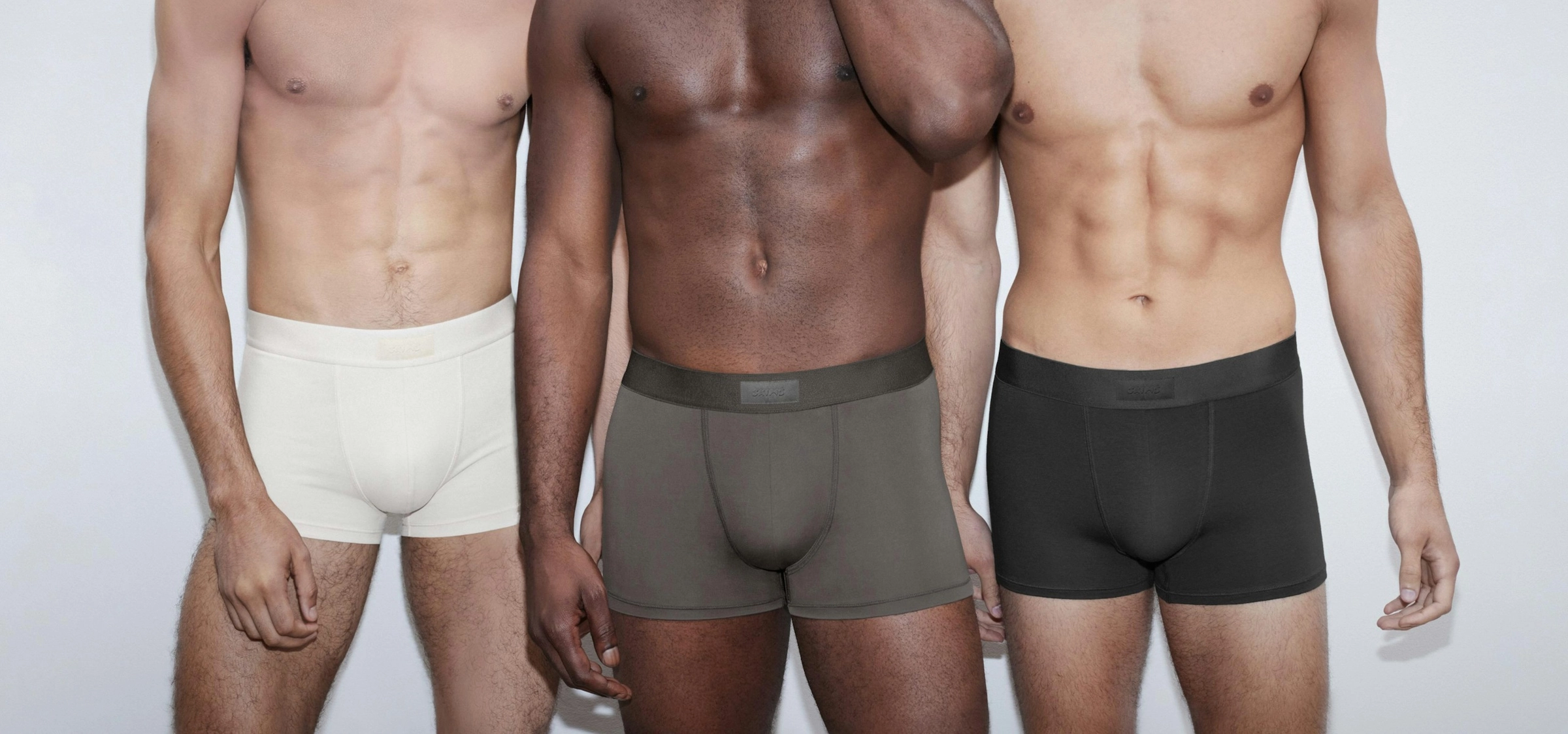 Three men in cream, taupe and black boxer briefs stand side by side
