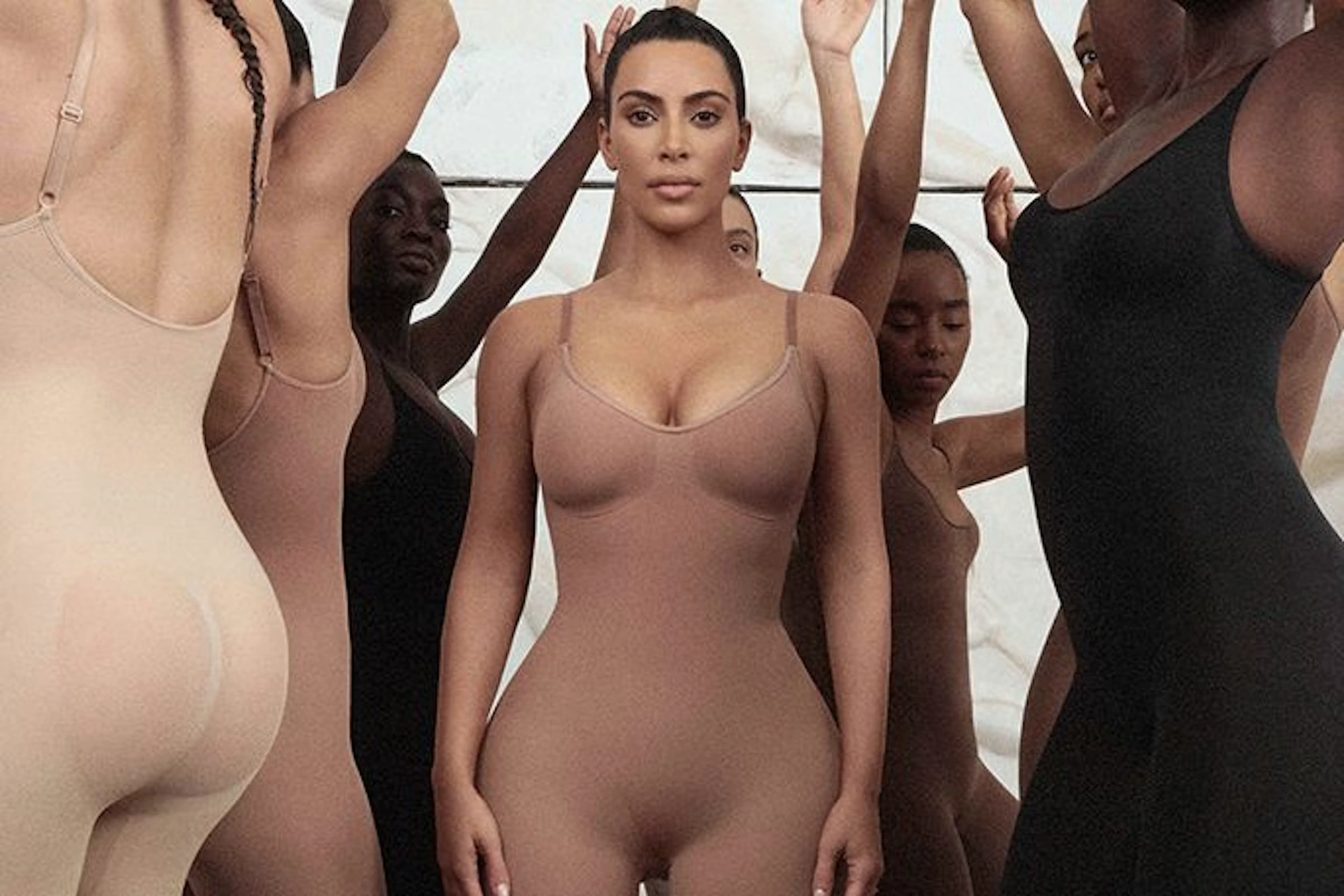 Models in nude shapewear bodysuits with arms raised against a wall