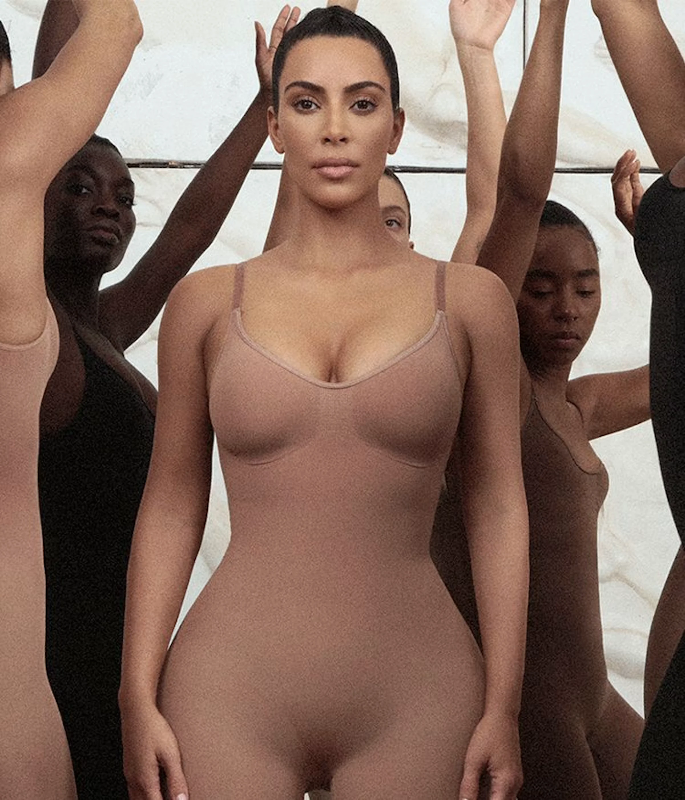 A model in a nude shapewear bodysuit with her arms raised