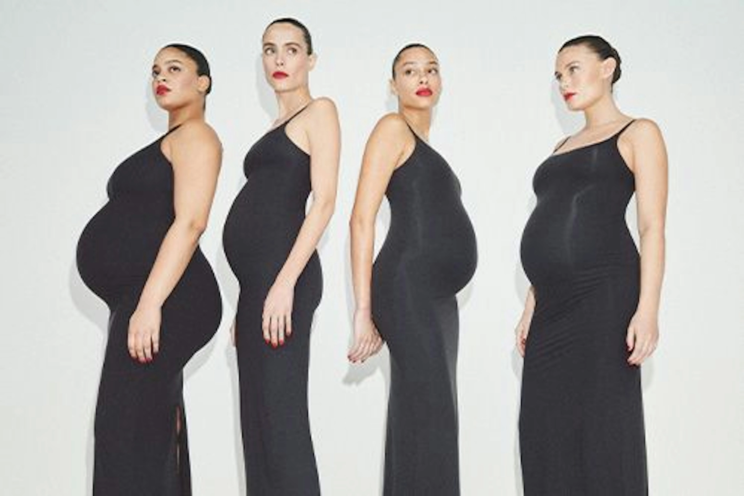 Four pregnant models in black fitted dresses stand in a row